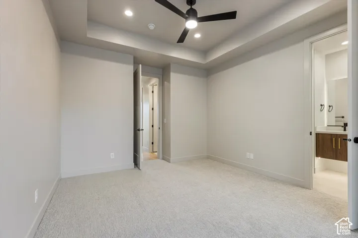 Recessed ceiling lighting, ceiling fan, tray ceiling, light-toned carpet flooring, and a bathroom entry with vanity