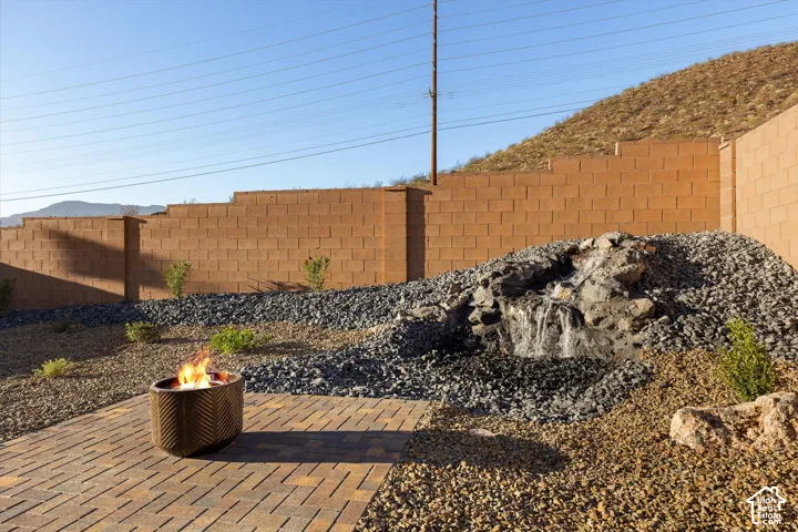 Paver patio with a decorative fire pit, a tiered rock water feature, and a textured block wall