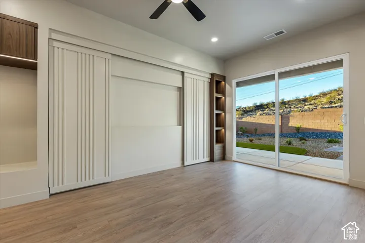 Wood-finish flooring, recessed lighting, ceiling fan, built-in shelving with accent lighting, and a sliding glass door to the exterior