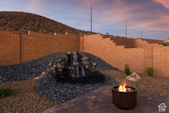 Paver patio featuring a stone-clad waterfall, integrated fire pit, and gravel landscaping with a block retaining wall