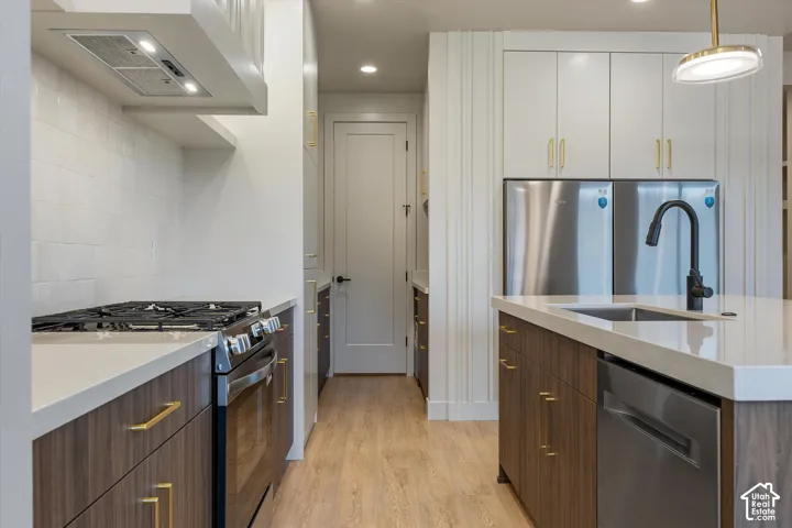 Gourmet kitchen featuring a stainless steel range, built-in range hood, white subway tile backsplash, wood-finish flooring, and a large island with an undermount sink