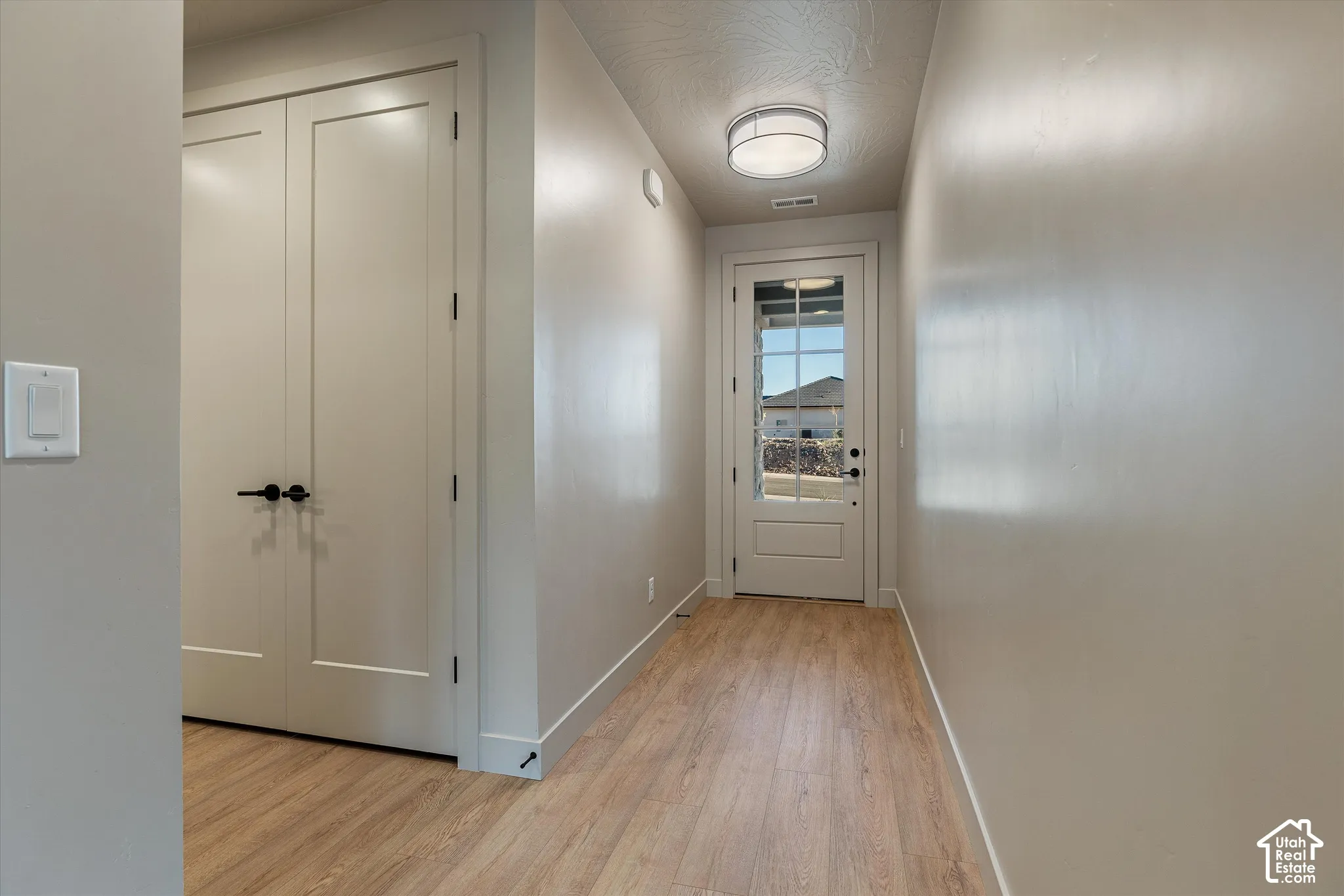 Wood-finish flooring with light-toned walls, a flush-mount ceiling light, and a panel-style door with a half-lite window