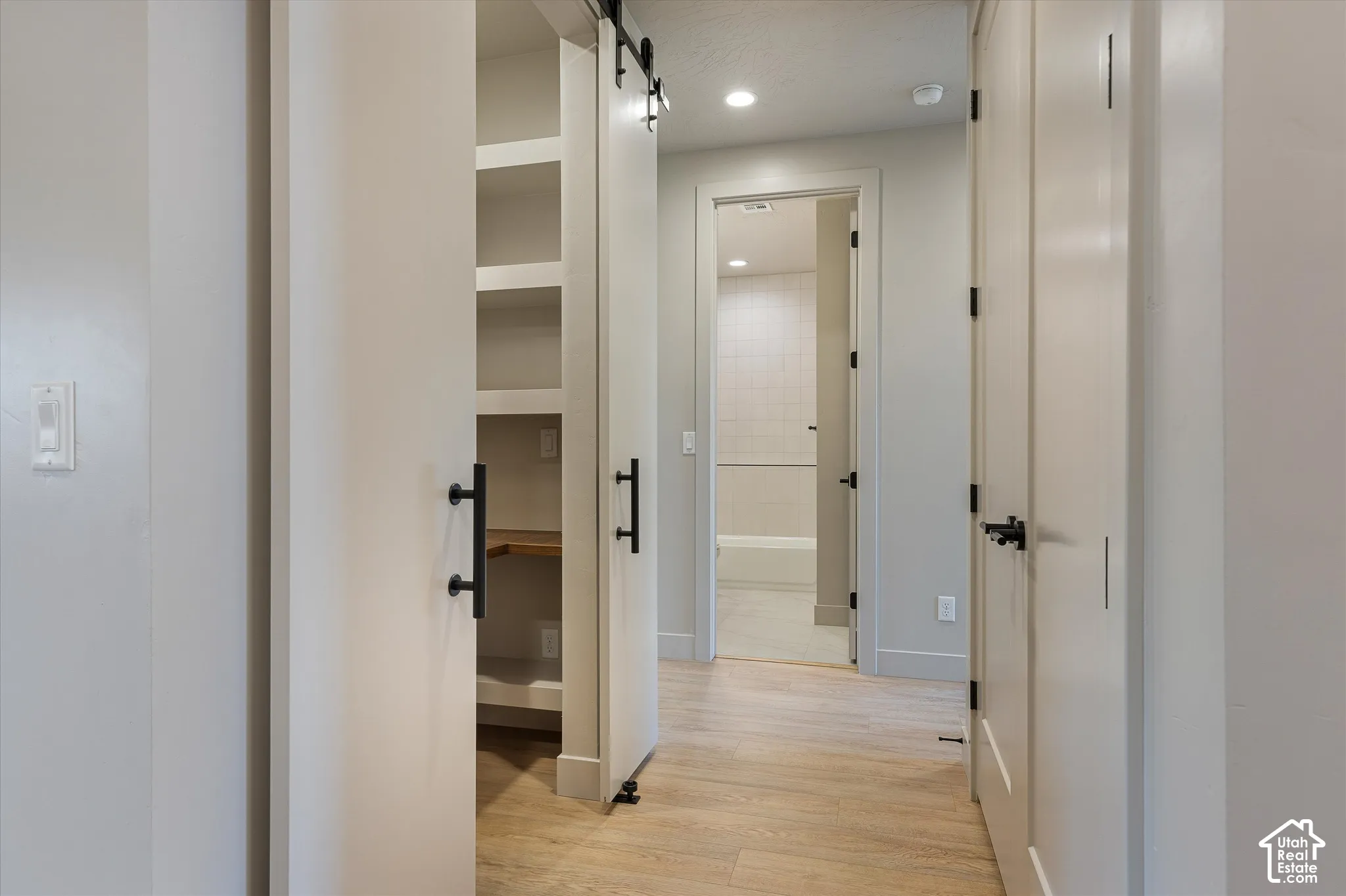 Hallway featuring wood-finish flooring, recessed lighting, white walls, and a barn door with black hardware