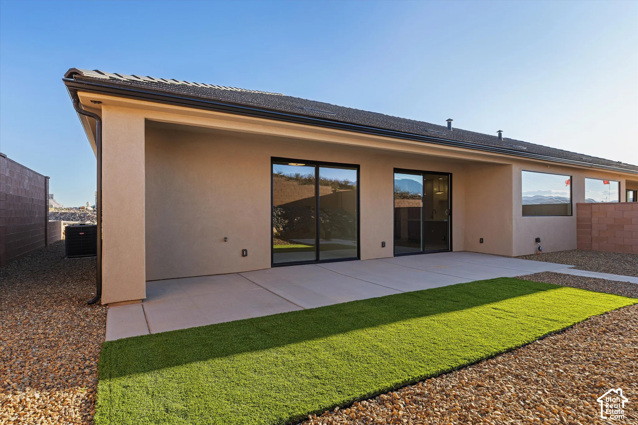 Expansive covered patio with concrete flooring, bordered by artificial turf and gravel landscaping