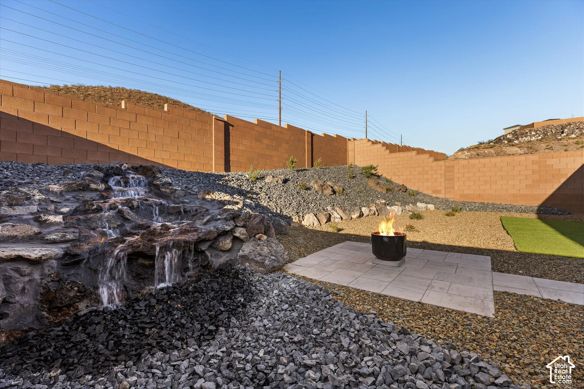 Stone water feature, paver patio, fire pit, artificial turf, and a block wall perimeter