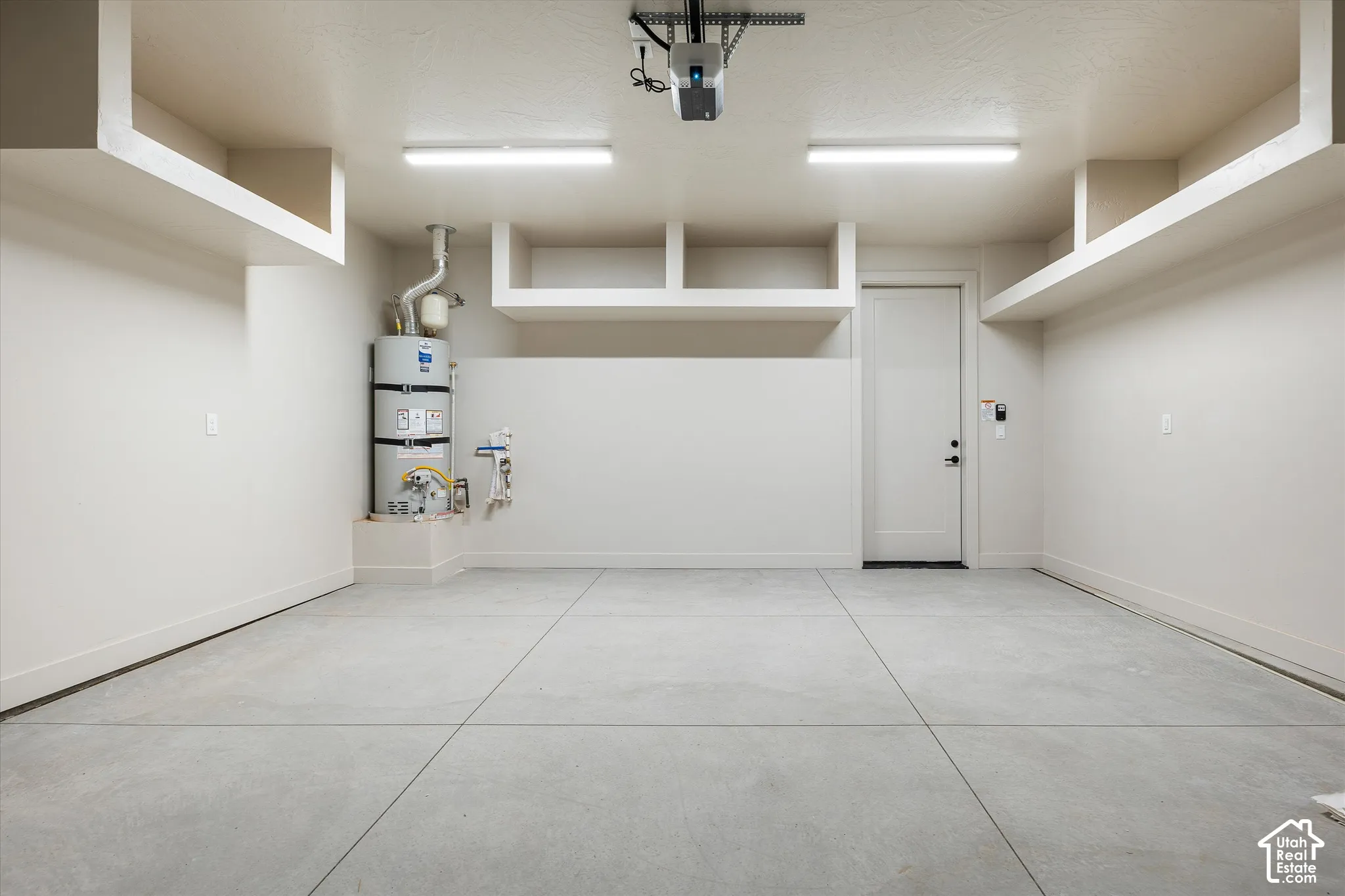 Concrete flooring in garage featuring overhead storage shelving, built-in water heater, and a white entry door