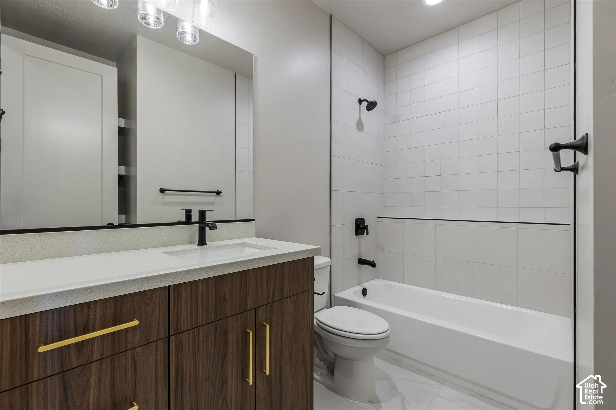Wood-finish vanity with gold-tone hardware, white countertop, integrated sink, and matte black faucet