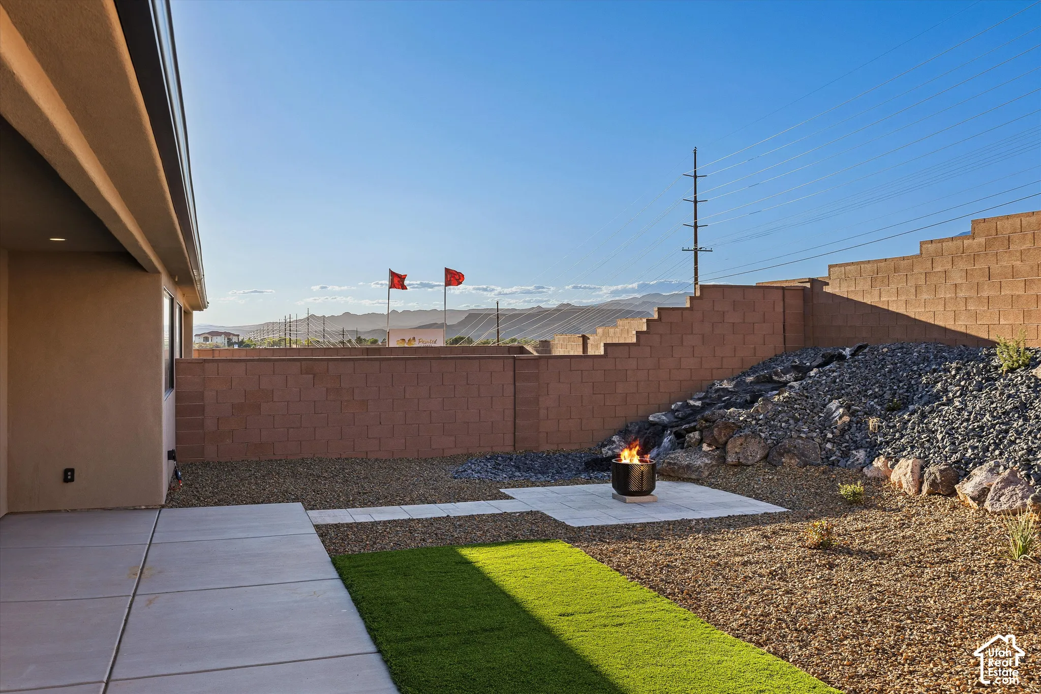 Expansive backyard featuring a concrete patio, artificial turf, decorative rock landscaping, and a built-in fire pit