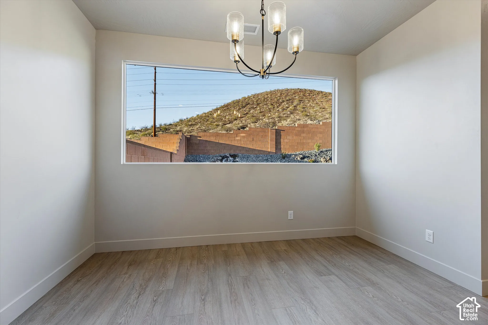 Spacious room featuring a wide picture window, wood-finish flooring, and a contemporary chandelier with glass shades