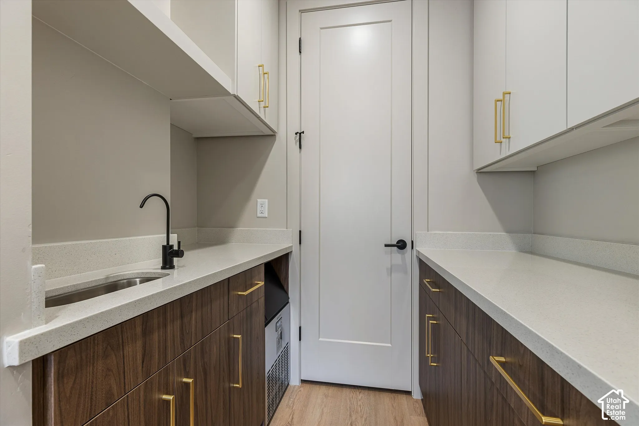 White panel door, wood-finish cabinetry with gold-tone hardware, light-toned countertops, undermount sink, and matte black faucet