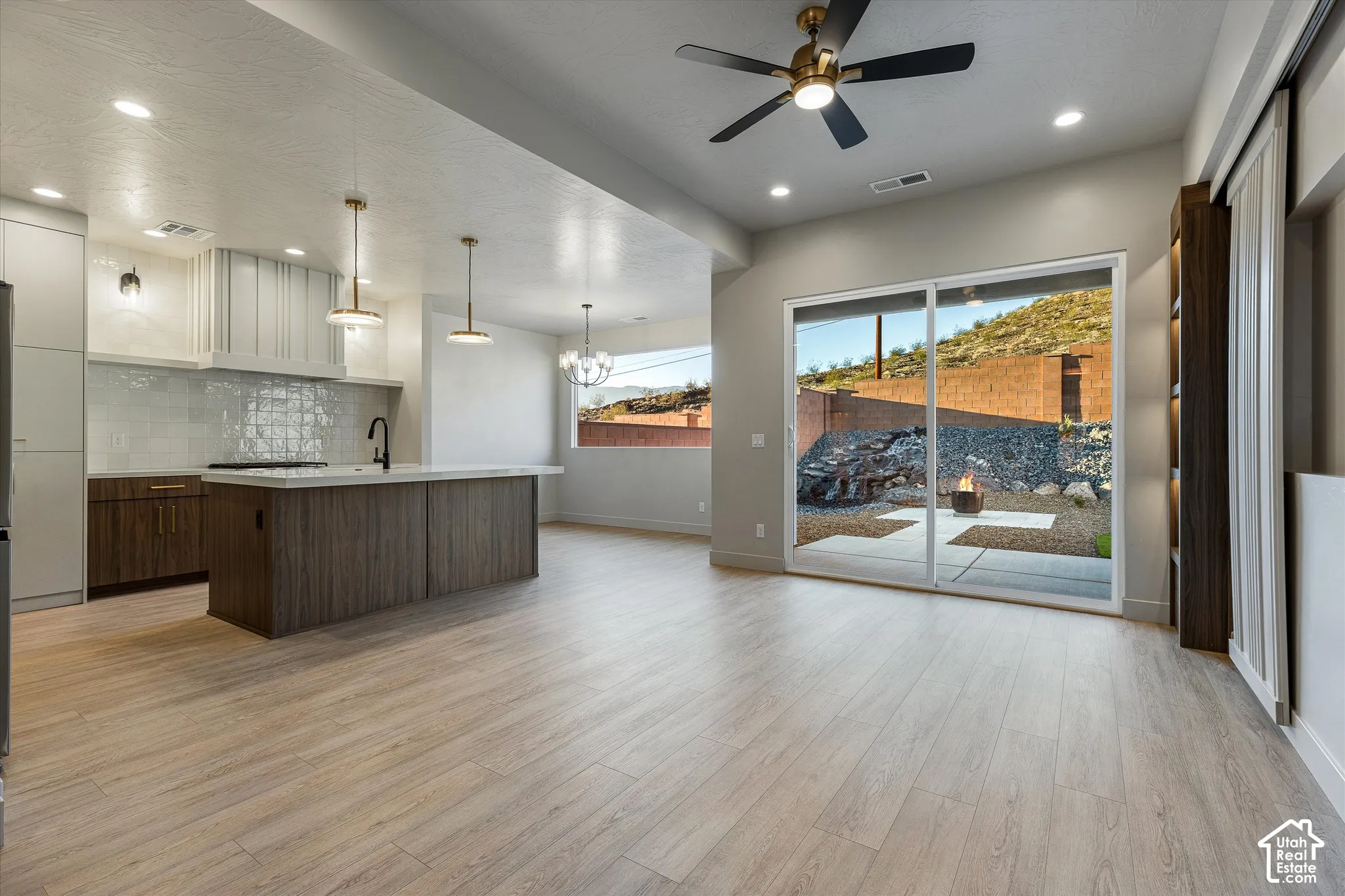 Open-concept living space with wood-finish flooring, a contemporary kitchen island, and a sliding glass door opening to a hardscaped outdoor area