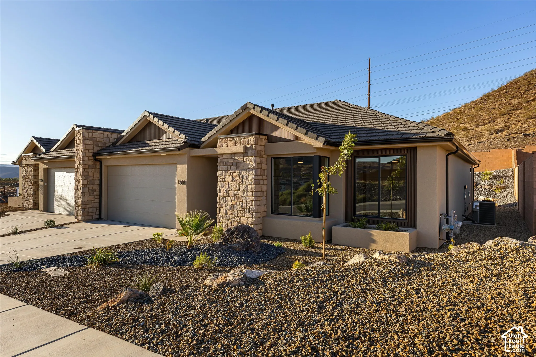 Stucco exterior with stone accents, a tiled roof, multi-pane windows, and a paved driveway leading to an attached garage