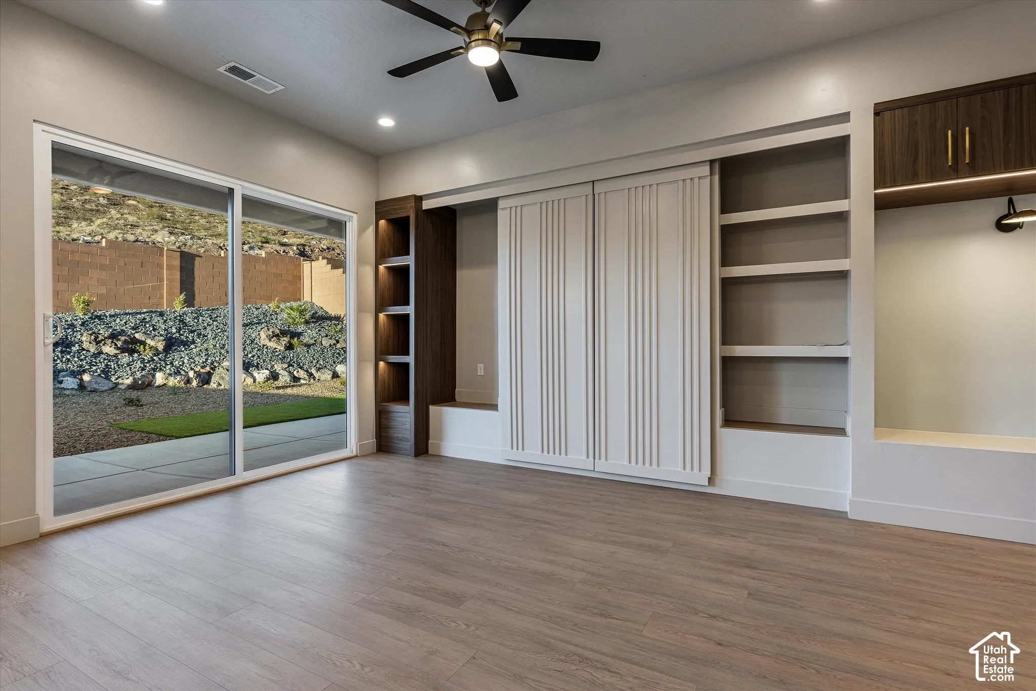 Wood-finish flooring, sliding glass door, built-in shelving, ceiling fan, and recessed lighting