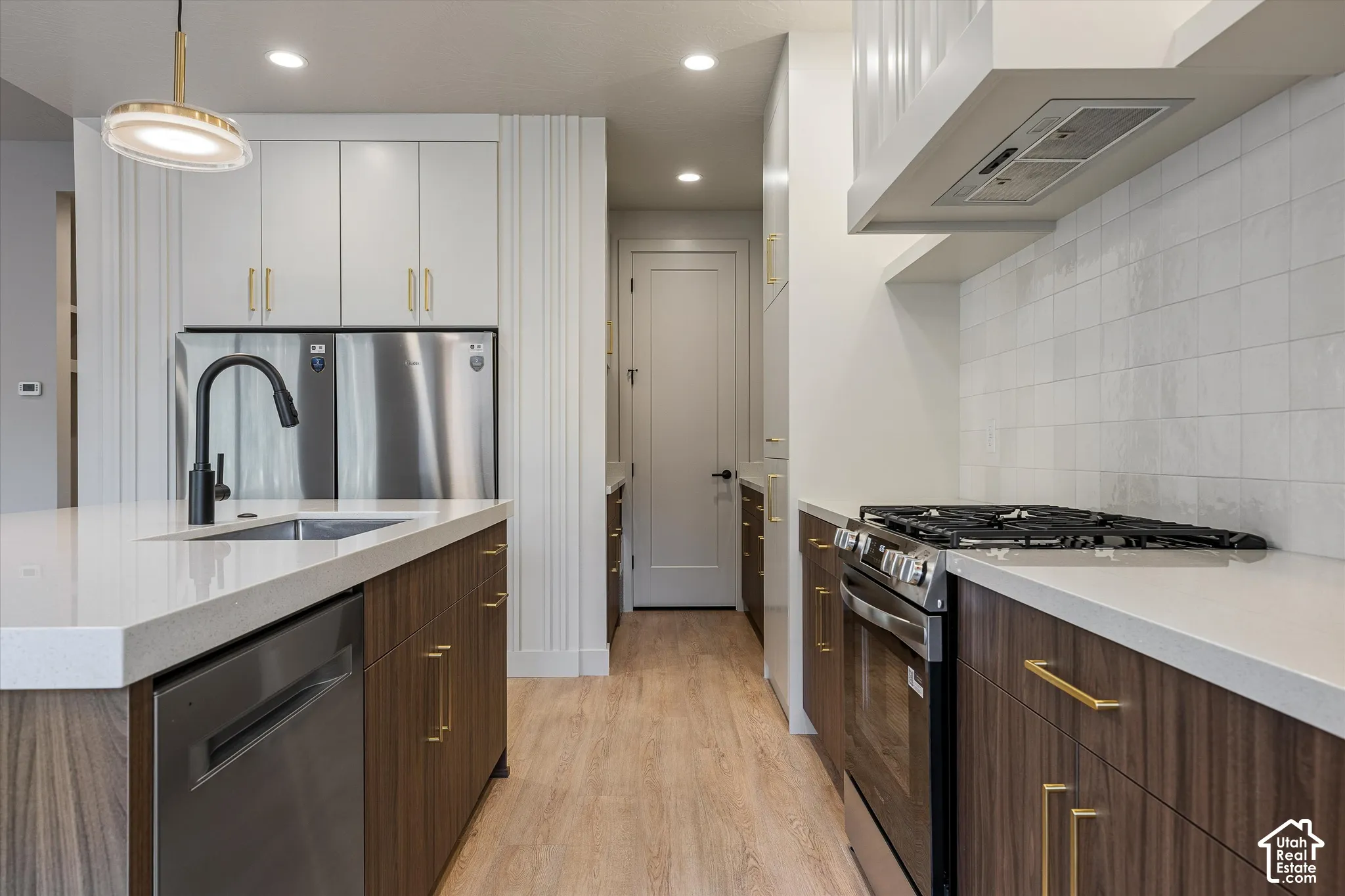 Modern kitchen featuring a gas range, stainless steel appliances, wood-finish cabinetry, light-toned countertops, and a tile backsplash