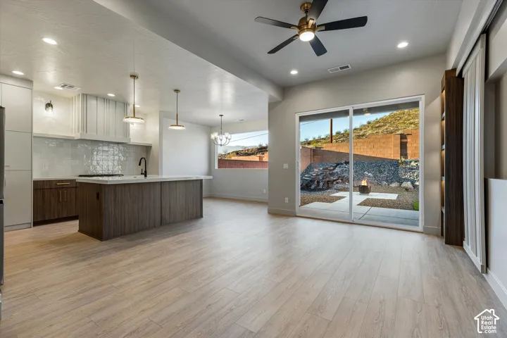 Open-concept living space with wood-finish flooring, a contemporary kitchen island, and a sliding glass door opening to a hardscaped outdoor area