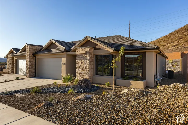Stucco exterior with stone accents, a tiled roof, multi-pane windows, and a paved driveway leading to an attached garage