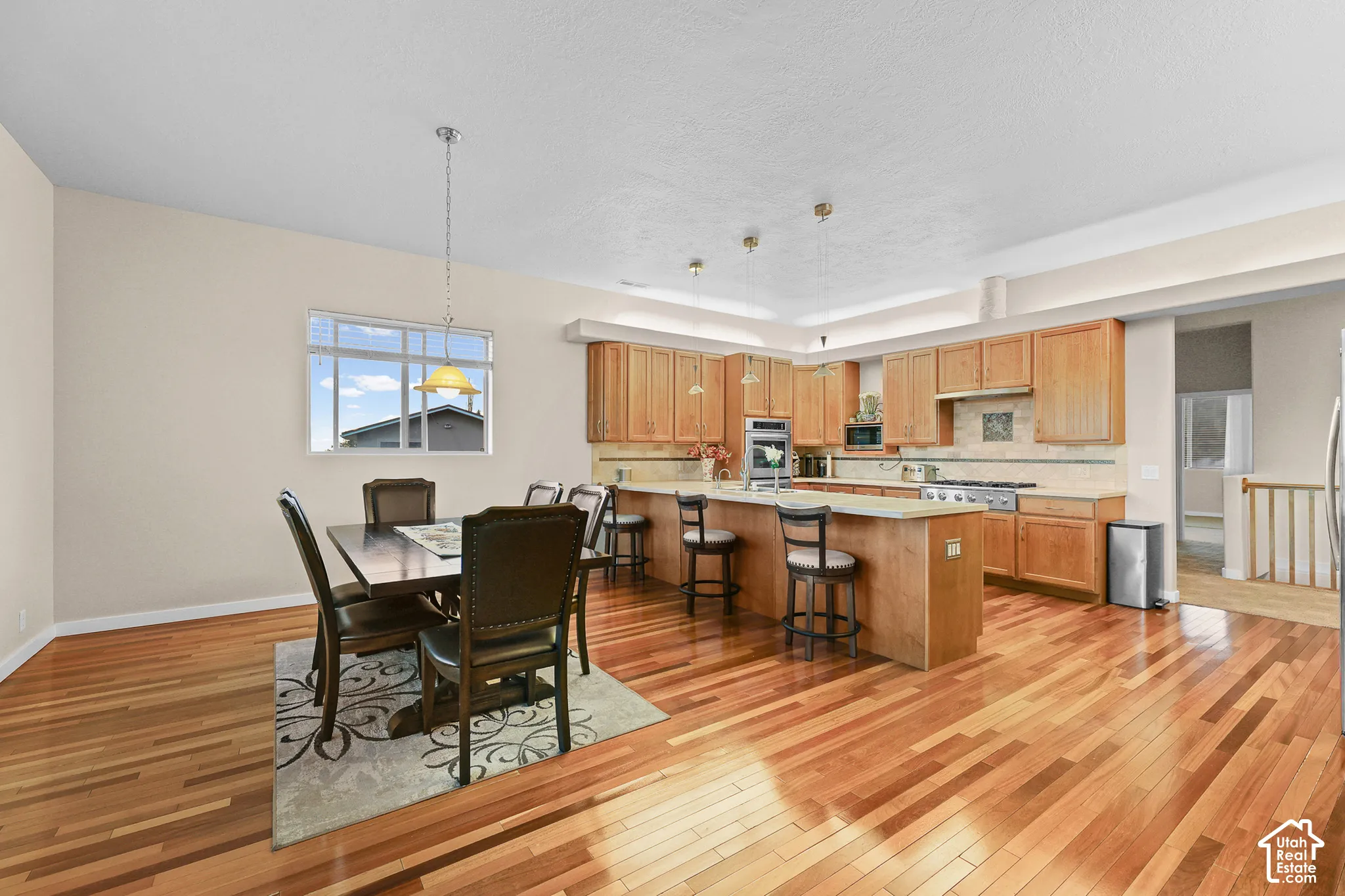 Wood-finish flooring throughout, featuring a kitchen with light wood cabinetry, a central island, and stainless steel appliances