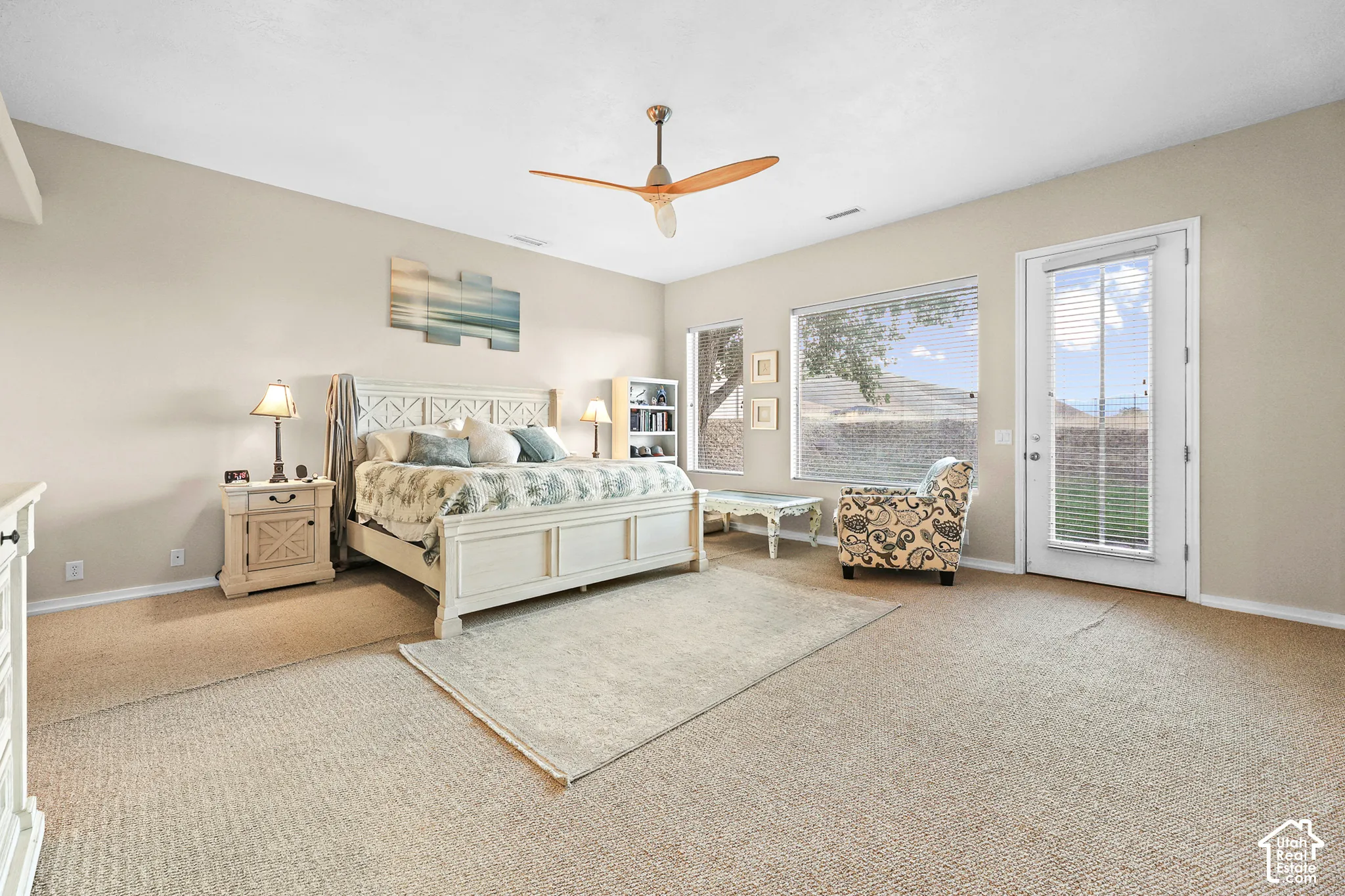 Spacious room featuring neutral carpet flooring, multiple windows providing natural illumination, and a ceiling fan with wood-finish blades