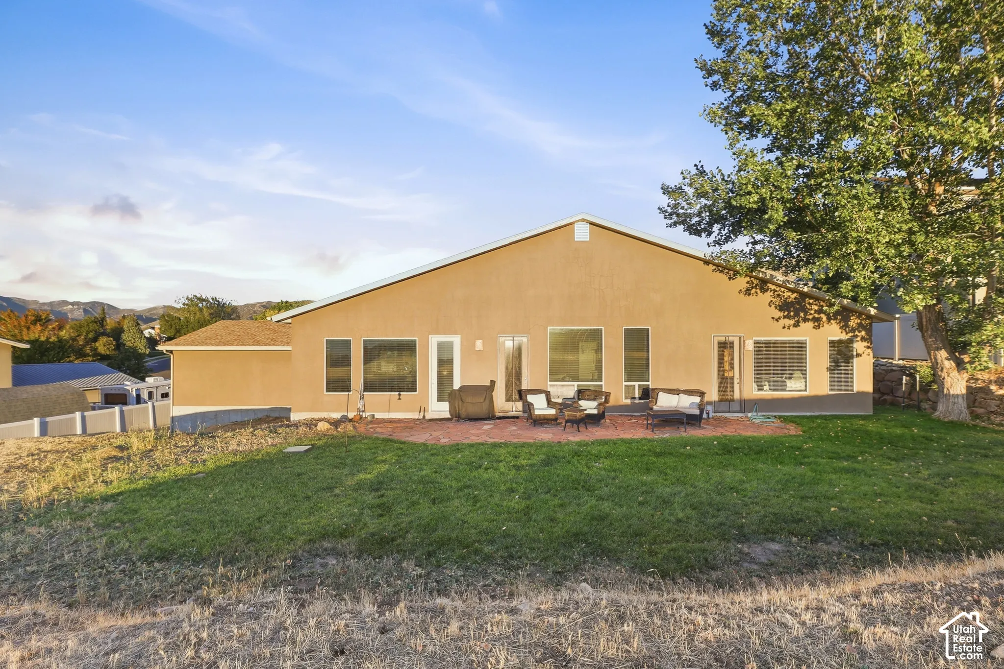 Stucco exterior with multiple large windows, a red brick patio, and a grass lawn