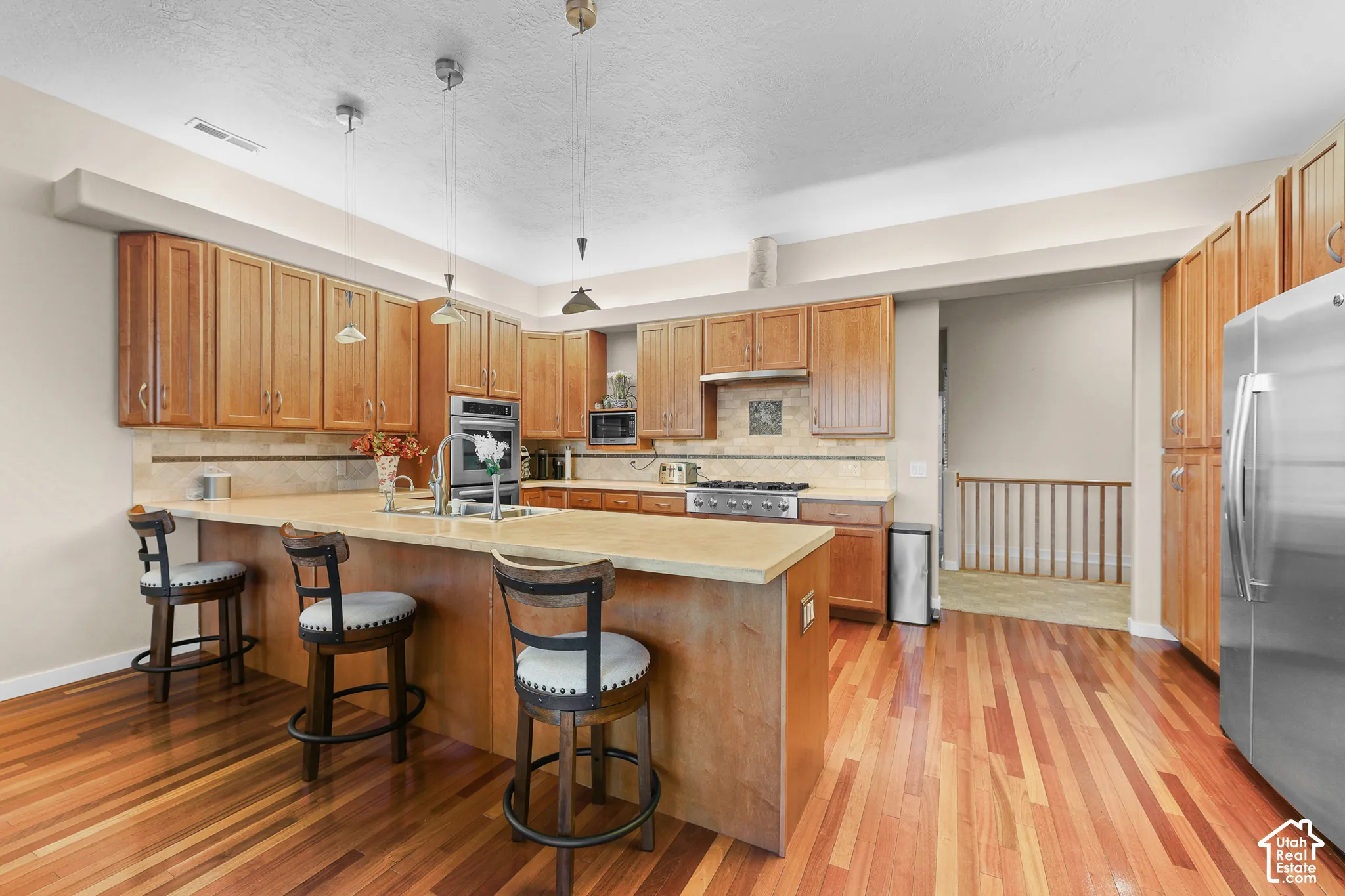 Hardwood flooring, light wood cabinetry, stone countertops, stainless steel appliances, and a kitchen island with seating
