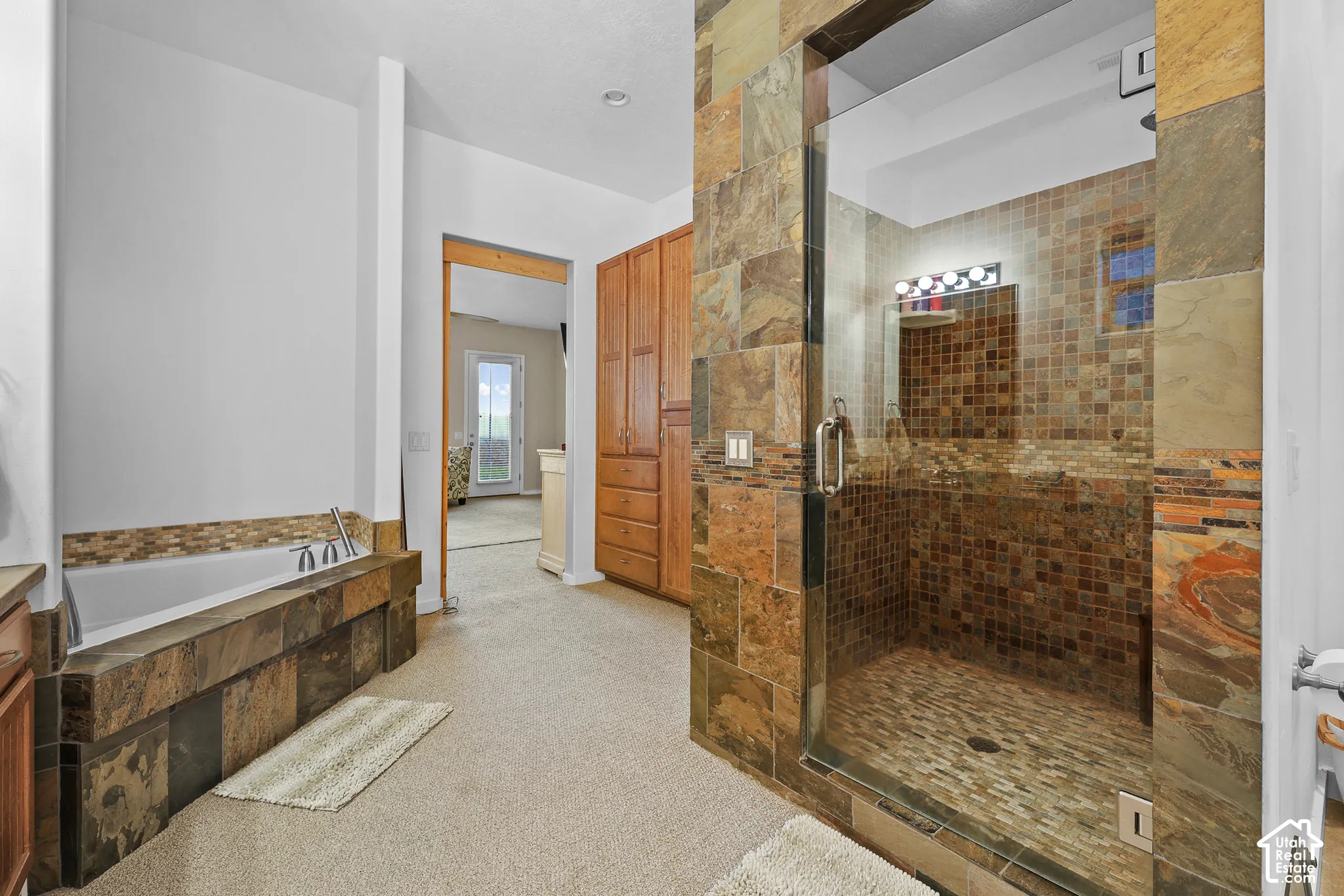 Spacious shower with glass enclosure and mosaic tile, built-in bathtub with tile surround, and wood cabinetry