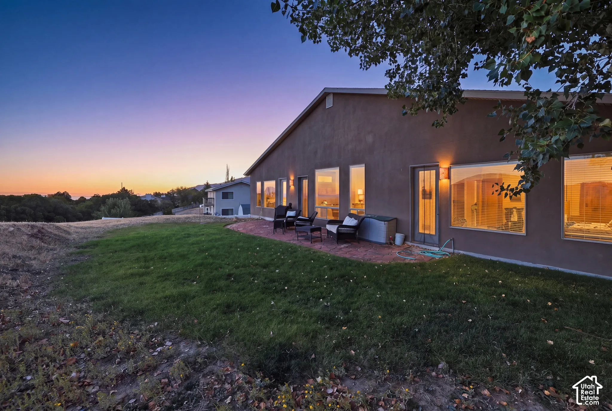 Expansive backyard with a manicured lawn, brick patio, and numerous windows