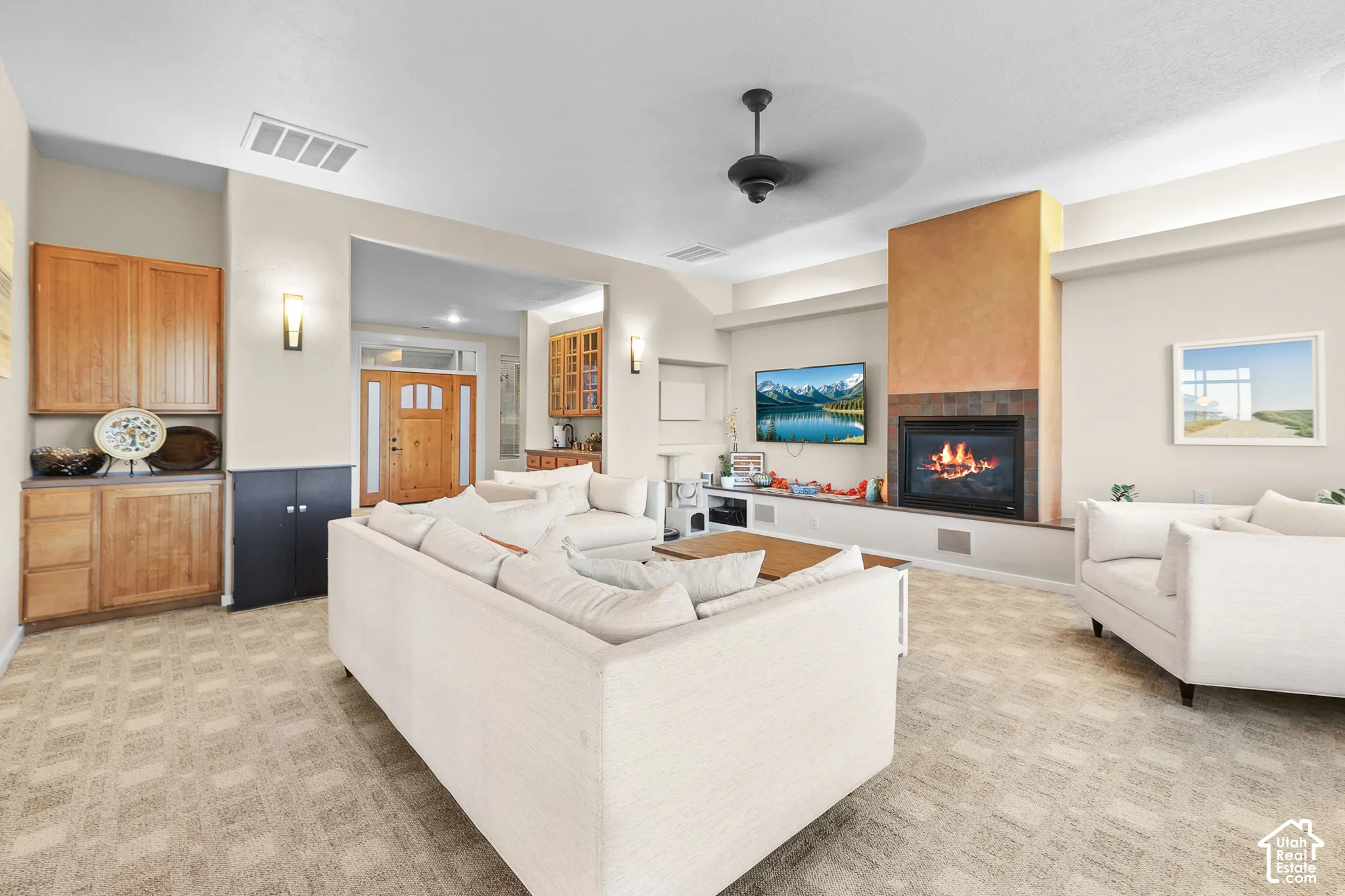Living area featuring a floor-to-ceiling fireplace with stone surround, a ceiling fan, patterned carpet flooring, and integrated built-in cabinetry