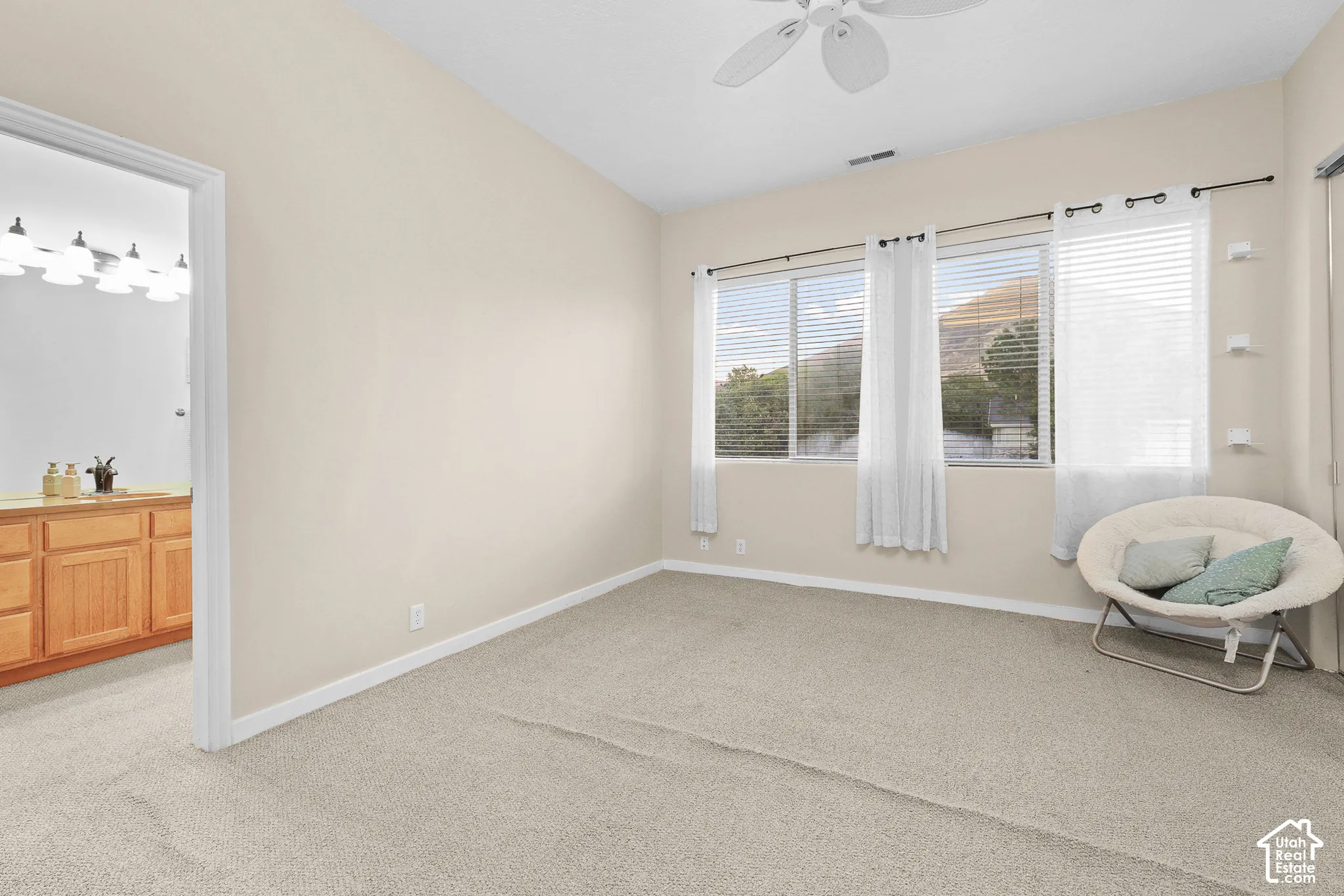 Ceiling fan with light fixture, wall-to-wall carpeting, multiple windows with blinds, recessed shelving, and a vanity with wood cabinetry