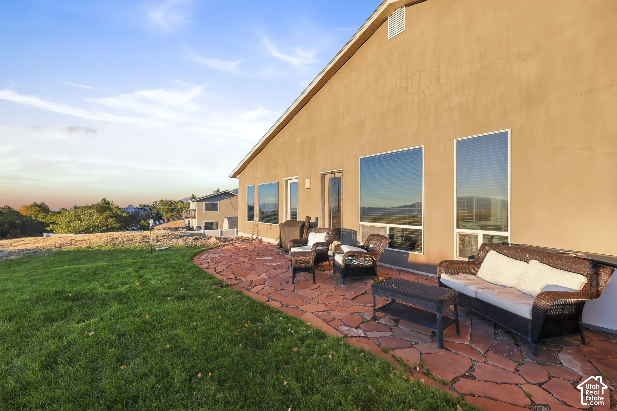 Expansive backyard featuring a natural stone patio, stucco exterior, multiple large windows, and a glass-paneled exterior door