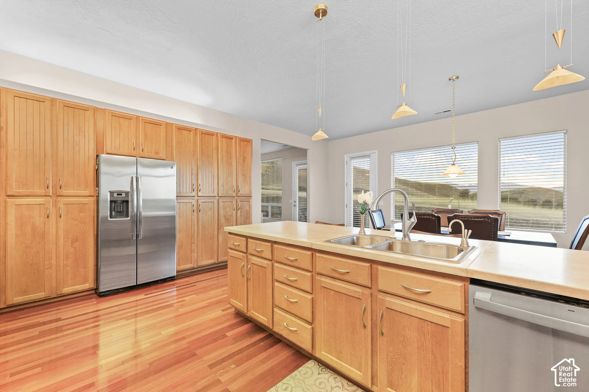 Kitchen featuring extensive wood cabinetry, wood-finish flooring, a stainless steel refrigerator, and a kitchen island with a double basin sink