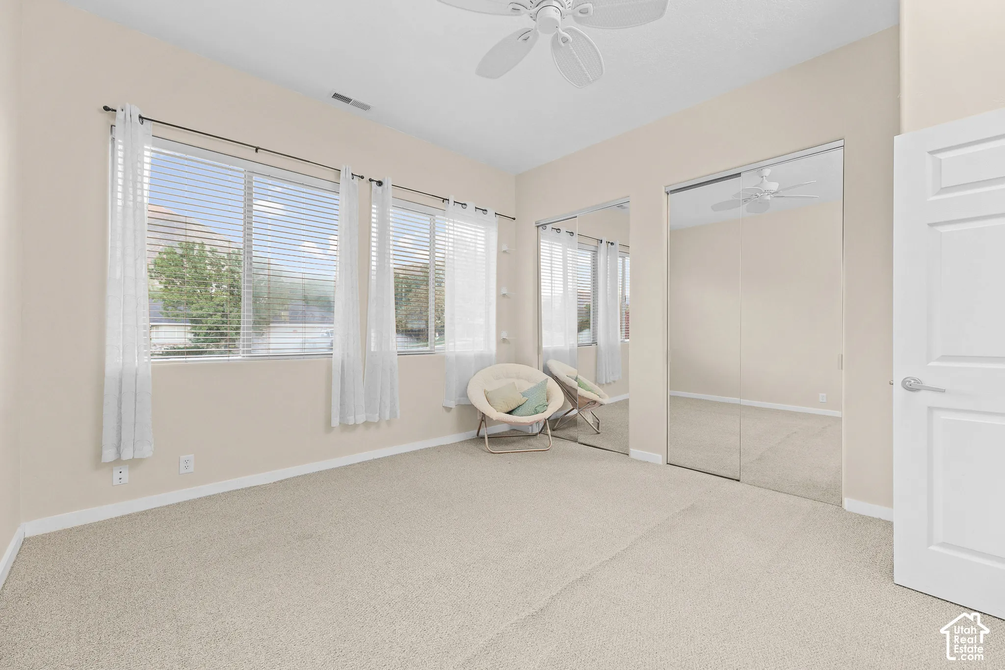 Angled ceiling with a ceiling fan, multiple windows with blinds, mirrored sliding closet doors, and light-colored carpeting