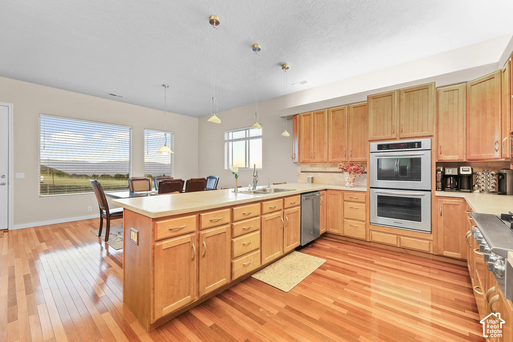 Kitchen featuring wood-finish flooring, a large central island, stainless steel double ovens, a built-in dishwasher, and ample wood cabinetry