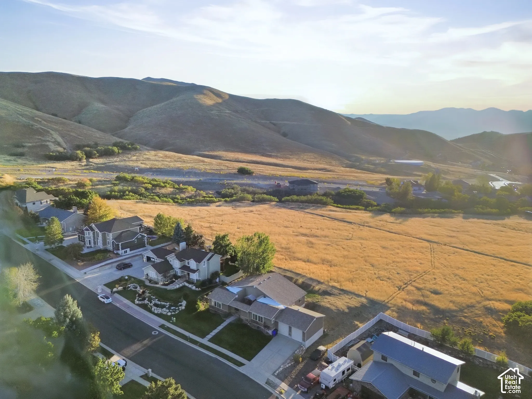 Expansive mountain backdrop with a residential street, featuring multiple homes with pitched roofs, and a large open field