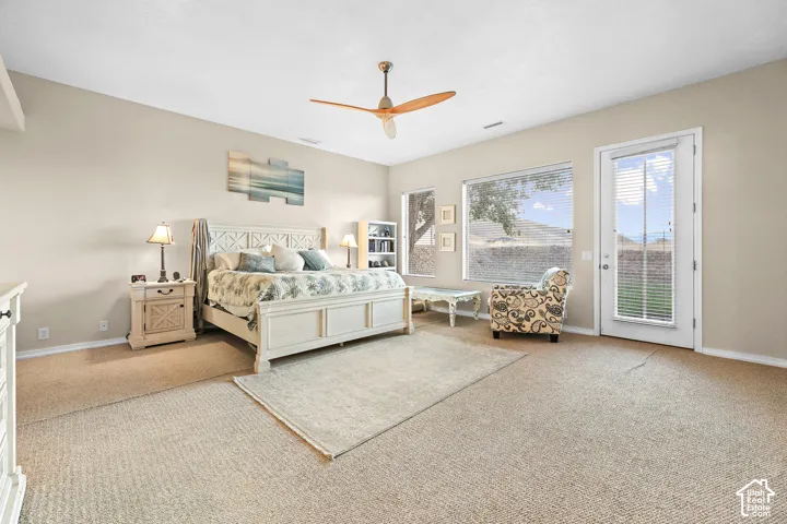 Spacious room featuring neutral carpet flooring, multiple windows providing natural illumination, and a ceiling fan with wood-finish blades