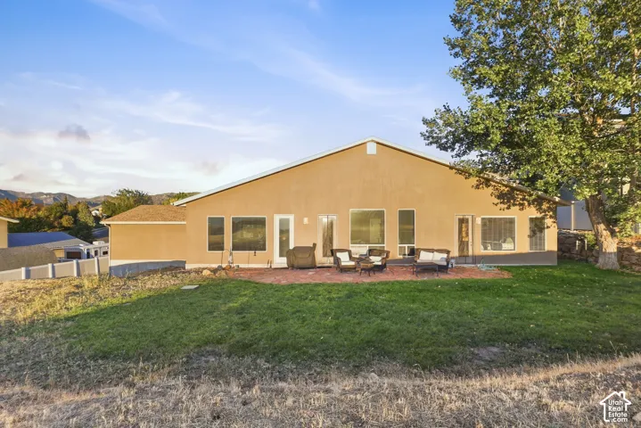 Stucco exterior with multiple large windows, a red brick patio, and a grass lawn