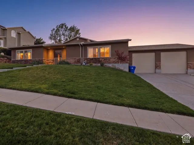 Split-level residence featuring a stucco exterior with stone accents, an attached two-car garage, a concrete driveway, and a front lawn with a sidewalk