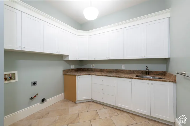 White shaker-style cabinetry with crown molding, stone-finish countertops, stainless steel sink with faucet, and tile flooring