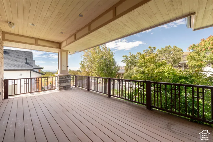 Expansive covered deck featuring composite wood-finish flooring, recessed lighting, and decorative metal railings
