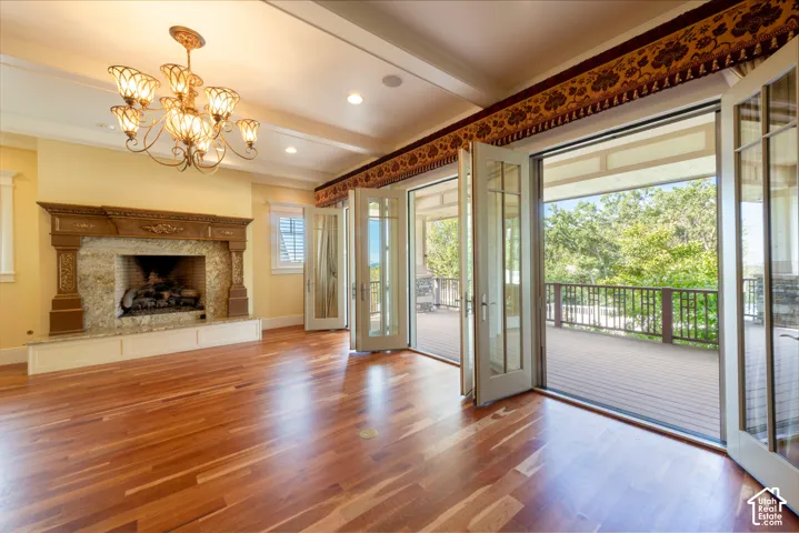 Hardwood flooring, ornate stone fireplace with carved wood mantel, multiple sets of glass French doors, decorative chandelier, and recessed lighting