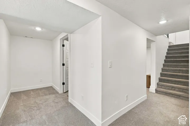 Carpeted flooring throughout, recessed lighting, white trim, and a white paneled door with dark hardware