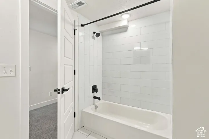 White subway tile shower surround with a matte black shower head and faucet, and a white bathtub.  Roomy bathroom.