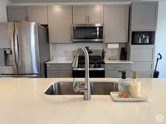 Stainless steel kitchen appliances, undermount stainless steel sink, brushed nickel faucet, light gray cabinetry, and white countertops