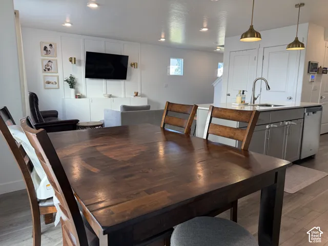 Integrated kitchen island with a stainless steel sink, wood-finish flooring, recessed lighting, and pendant light fixtures