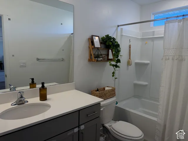 Vanity with an integrated sink and chrome faucet, full-width mirror, white bathtub with a shower kit, and a frosted transom window