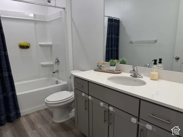 White integrated tub and shower unit, wood-finish flooring, grey vanity with silver hardware, white countertop, and an integrated sink with a chrome faucet