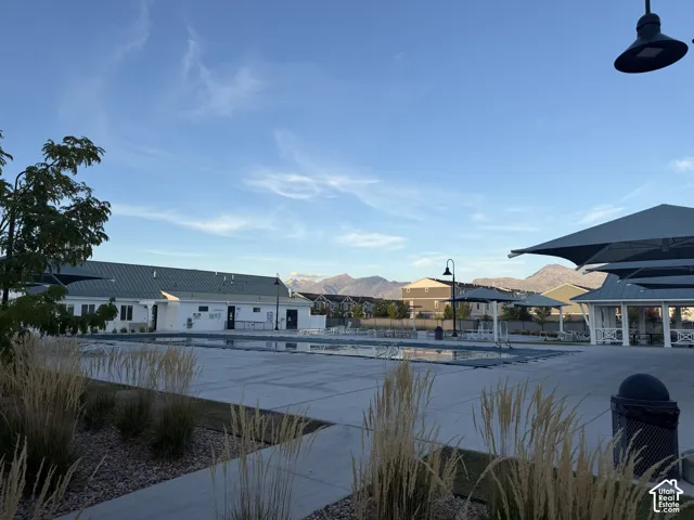 Expansive community pool area featuring a clubhouse, covered swimming pool, shade structures, and mountain backdrop