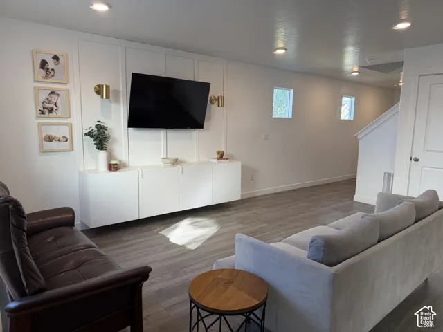 Recessed ceiling lighting, wood-finish flooring, white built-in cabinetry, wall-mounted sconces, and a staircase with white balusters