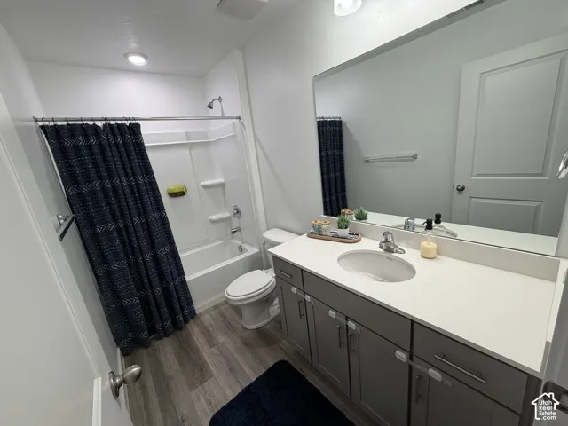 Bathroom featuring a single vanity with stone countertop, wood-finish flooring, a full-width mirror, and a tub-shower combination