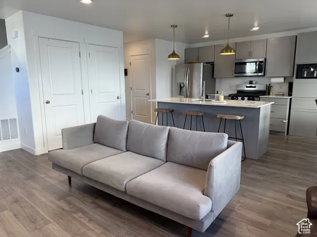 Open-concept living space with wood-finish flooring, a kitchen island with seating, stainless steel appliances, and pendant lighting
