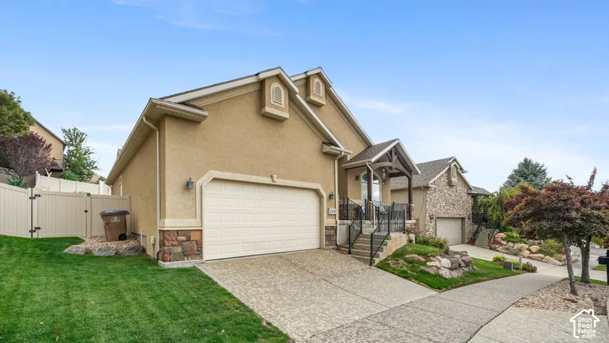Stucco exterior featuring stone accents, an attached garage, covered entryway, and mature landscaping